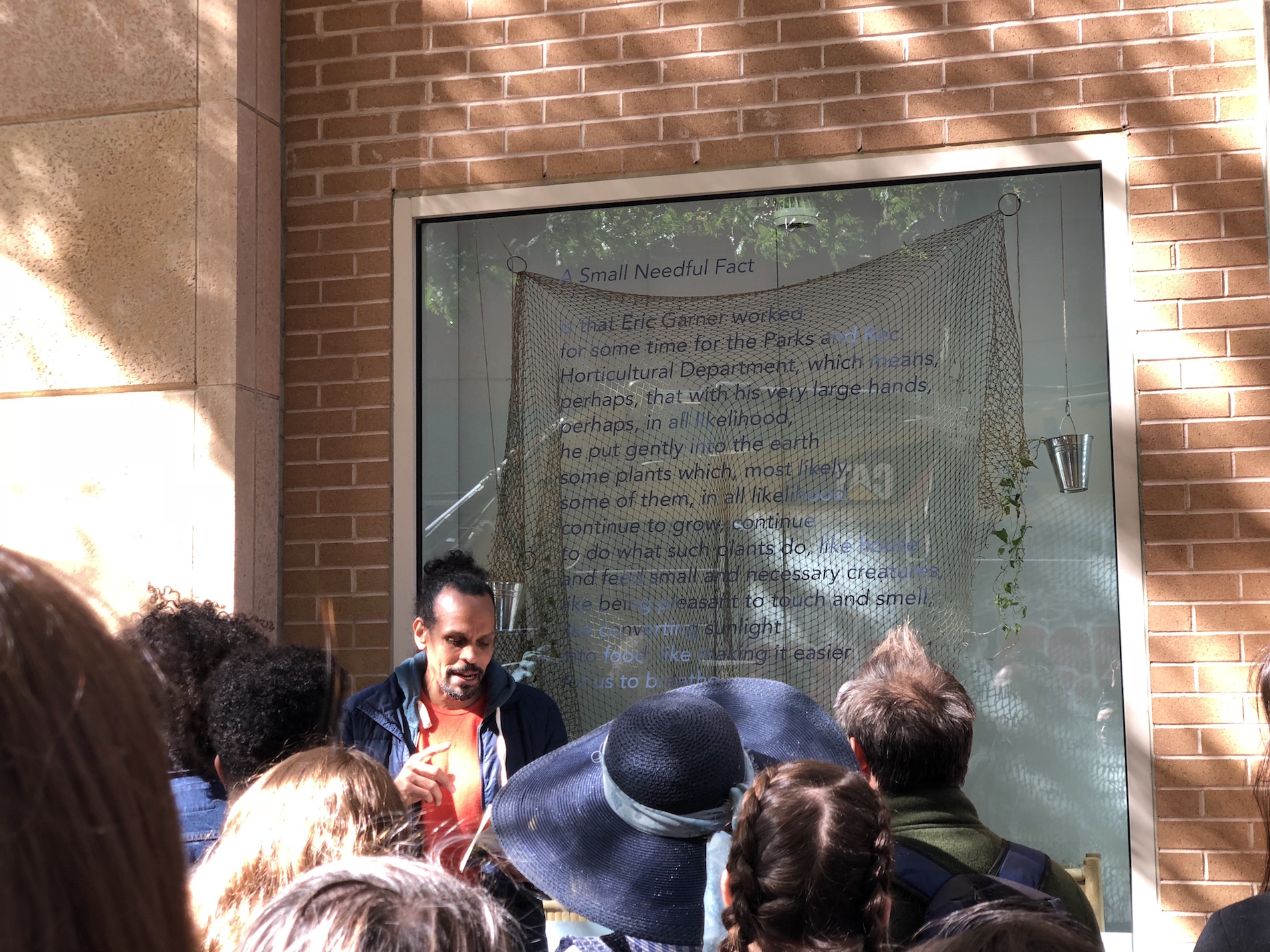 Ross Gay stands in front of window displaying his poem with an audience before him